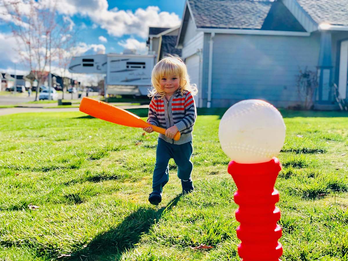 human boy holding orange bat walking toward red and white plastic pole toy people