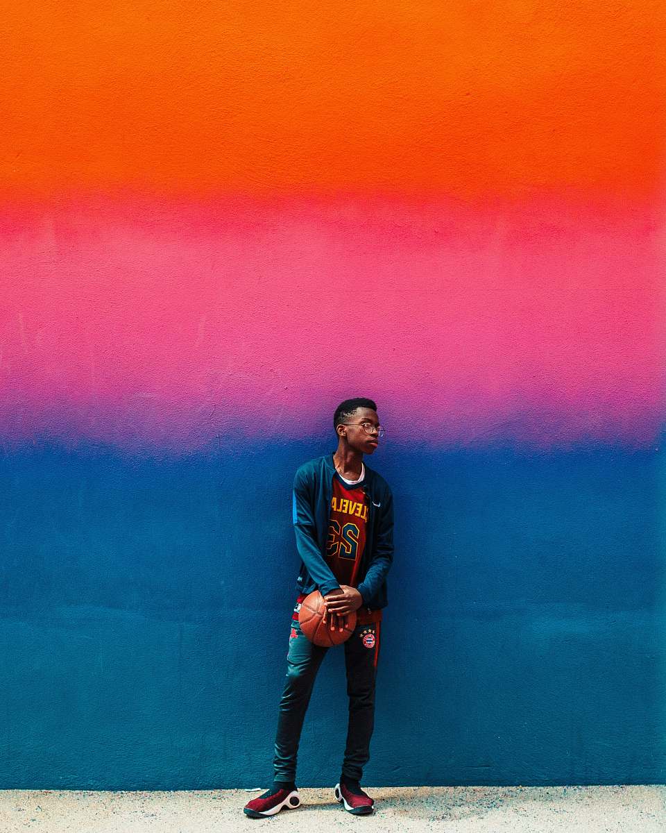 human boy standing and holding basketball beside blue and pink painted wall apparel