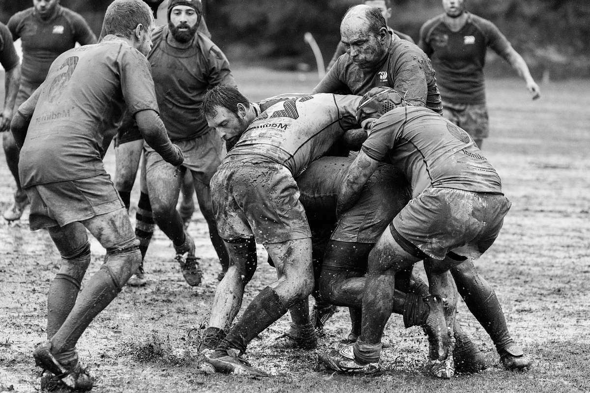 people grayscale photography of group of people playing rugby on muddy field black-and-white