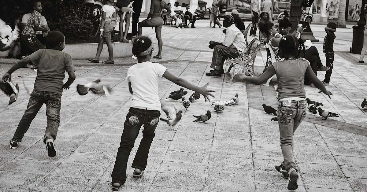 human grayscale photography of several kids running towards pigeons black-and-white