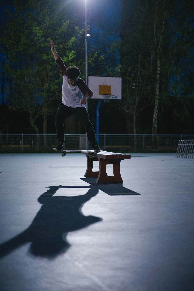 human man doing skateboard stunt on bench people