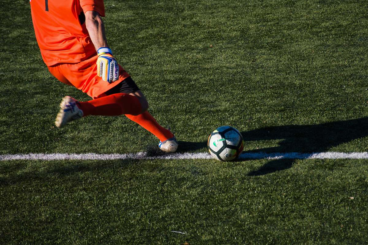 human man kicking soccer ball on field people