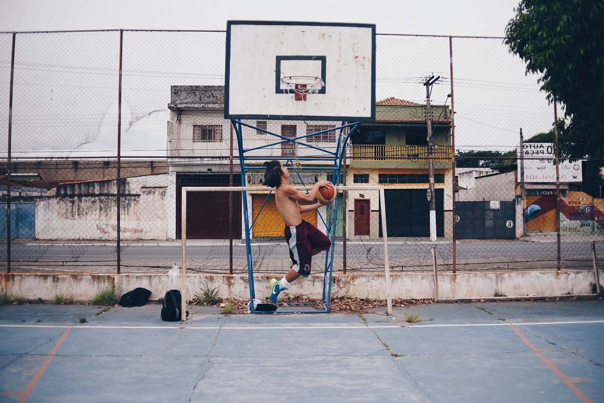 human man wearing brown shorts doing lay-up near basketball ring during daytime people