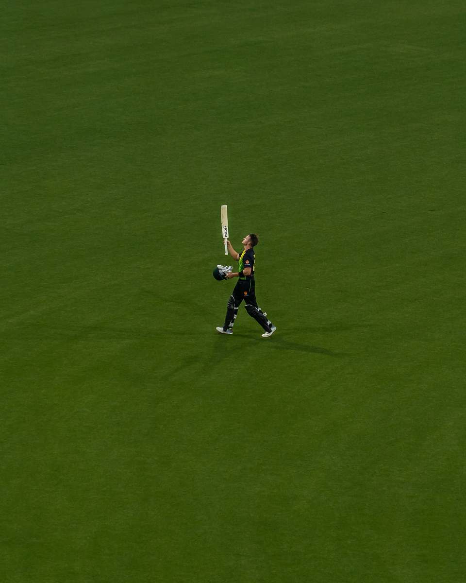 human person holding a cricket paddle in a green field people
