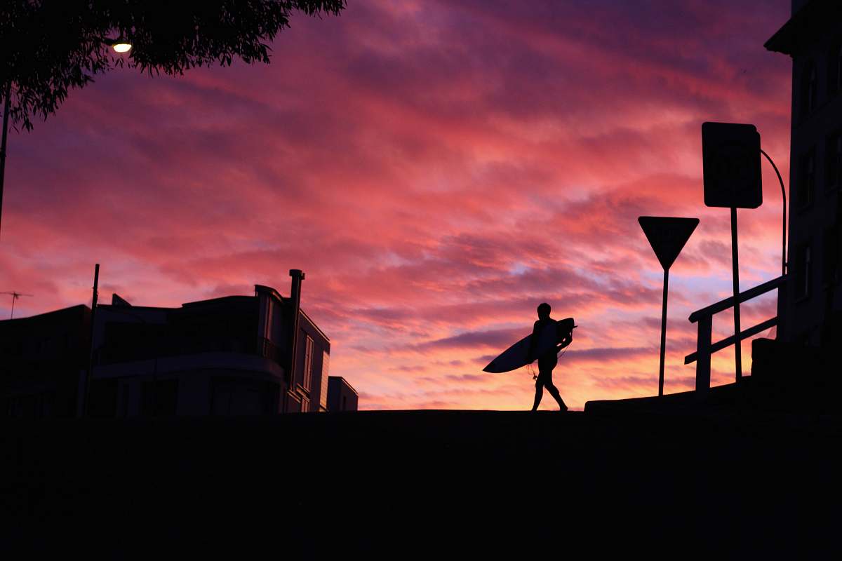 australia silhouette photography of man walking with a surfboard outdoors