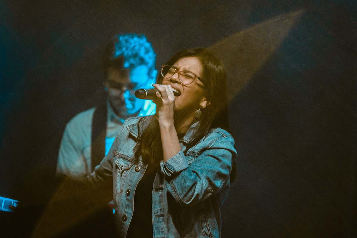 human woman wearing blue denim jacket singing near man playing guitar musical instrument