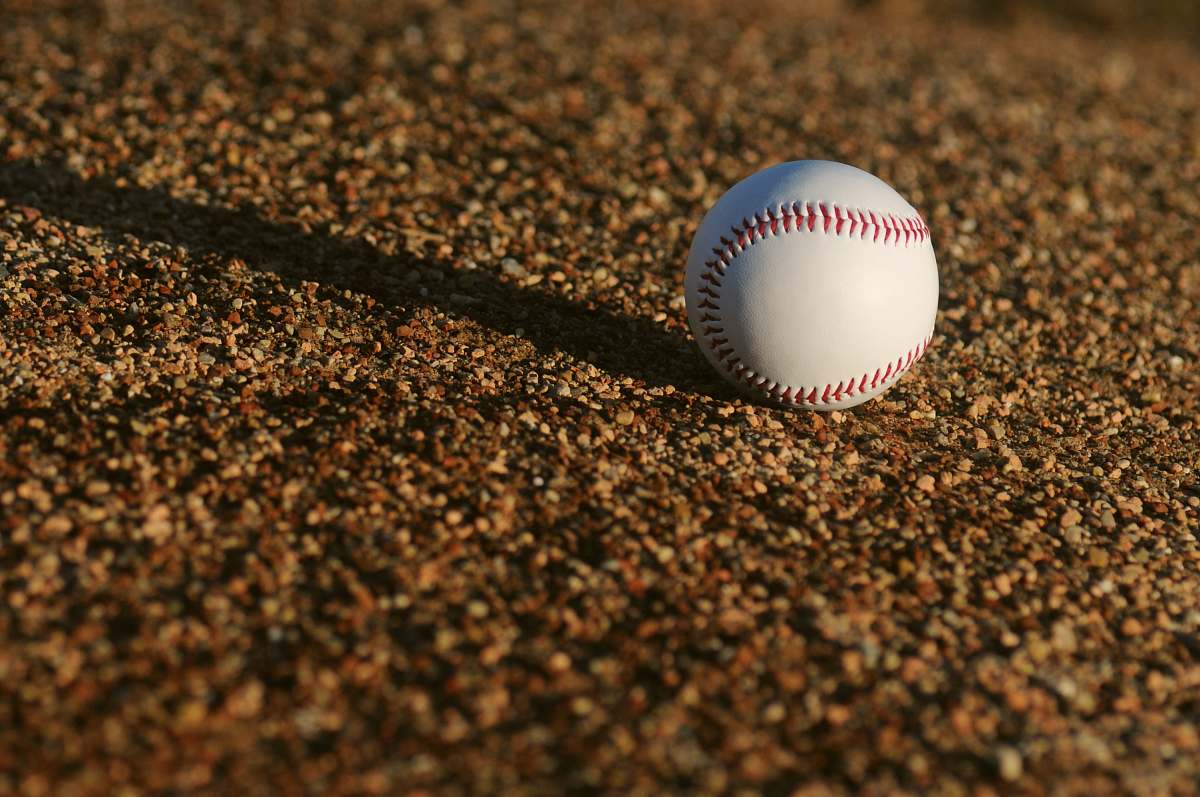 sports white and red baseball on brown soil at daytime baseball