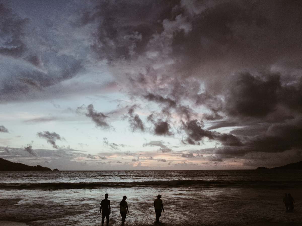 water silhouette of three people on seashore under gray cloudy skies sea