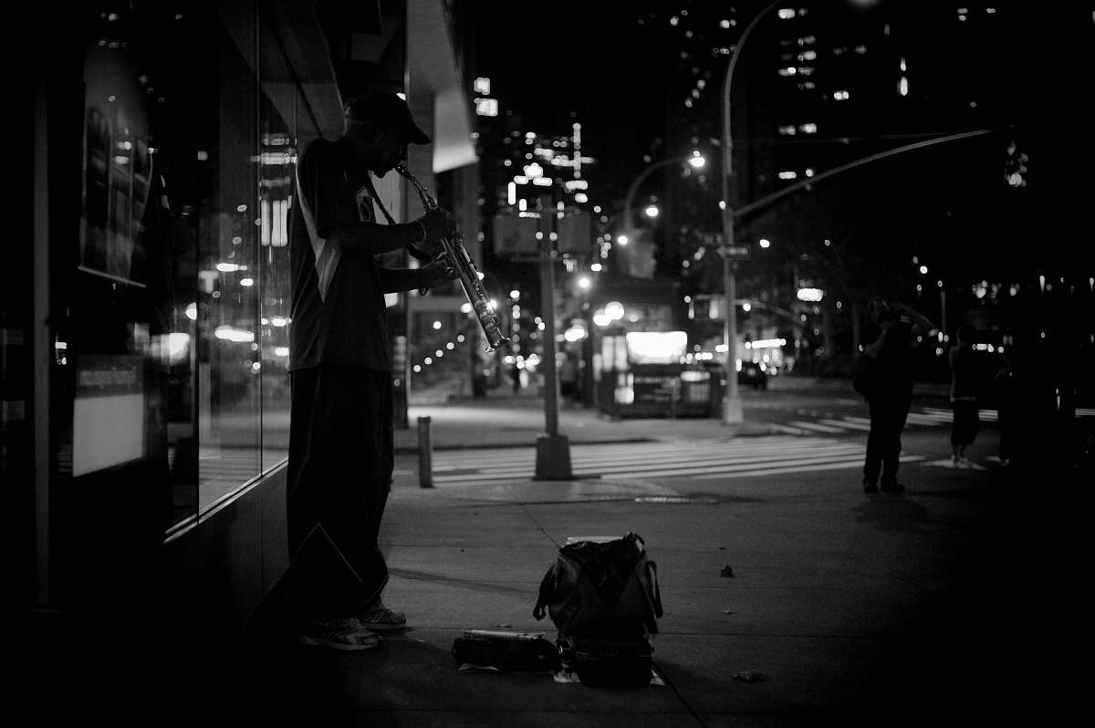 person grayscale photography of man playing musical instrument beside road human