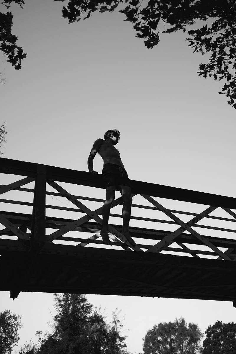 silhouette grayscale photography of man sitting on edge of bridge bridge