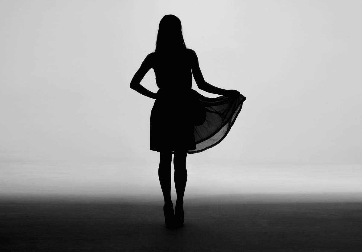 Capture the essence of sophistication with this striking silhouette of a woman gracefully holding the skirt of her black dress. Set in the middle of a softly lit room, this image evokes a sense of mystery and elegance, perfect for fashion-related projects, editorial spreads, or creative storytelling. Ideal for use in advertisements, blogs, or social media posts that highlight femininity, style, and grace.