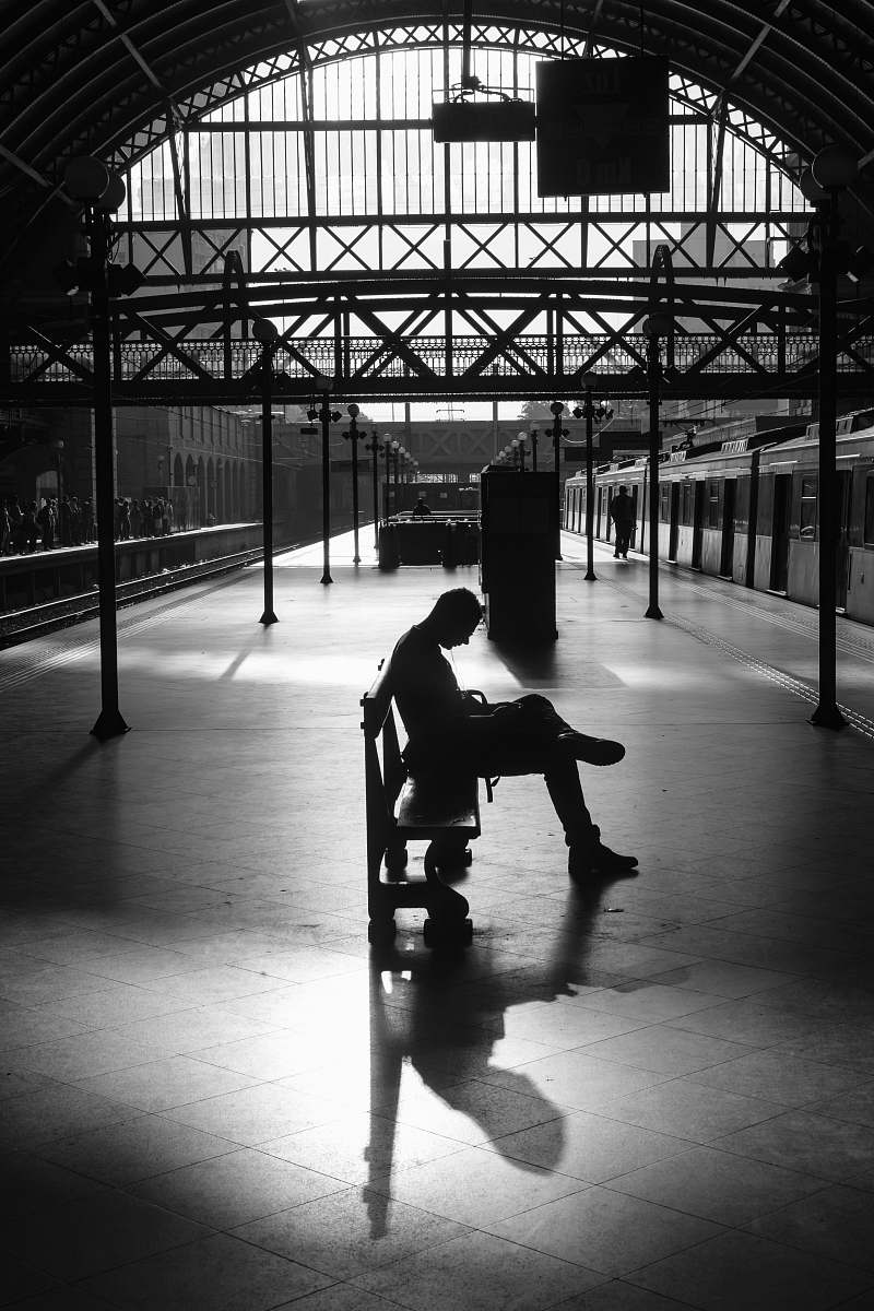 train silhouette photography of person sitting on bench terminal