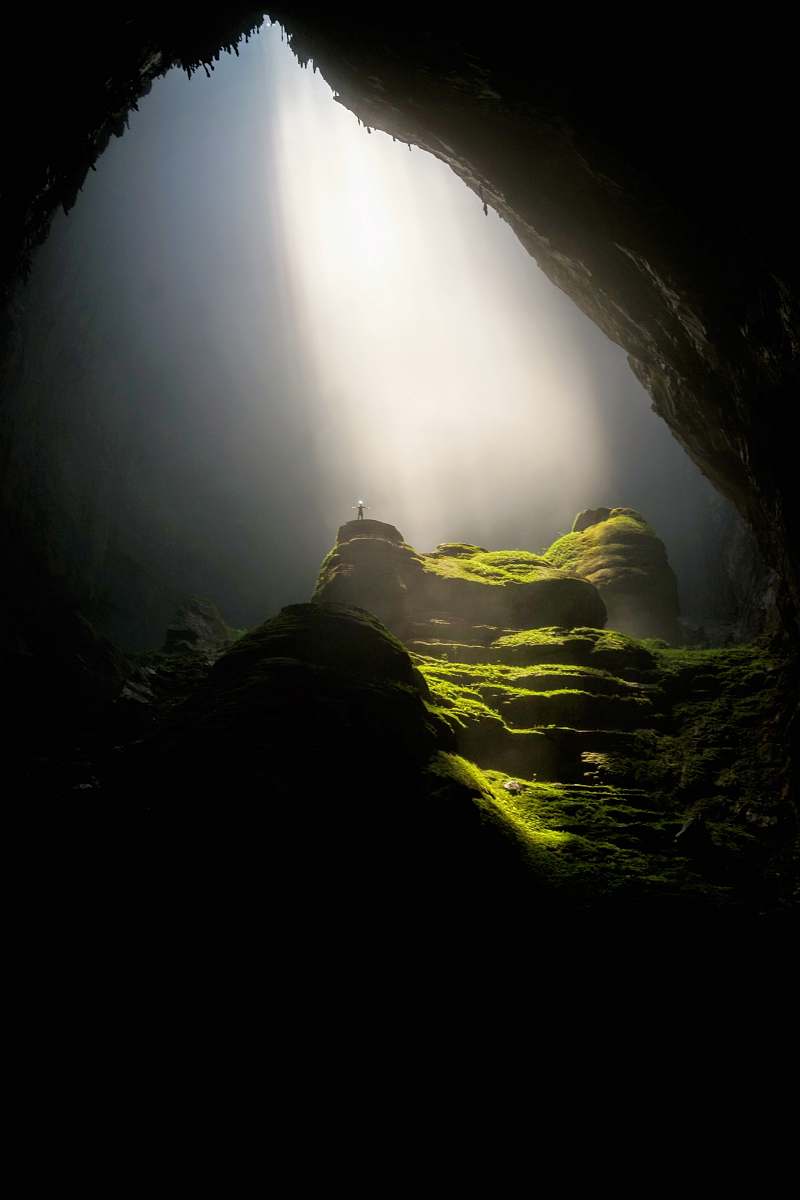 vietnam person on top of rock formation inside cave sun ray