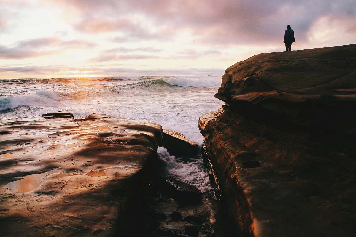 ocean person standing on a cliff facing body of water sea