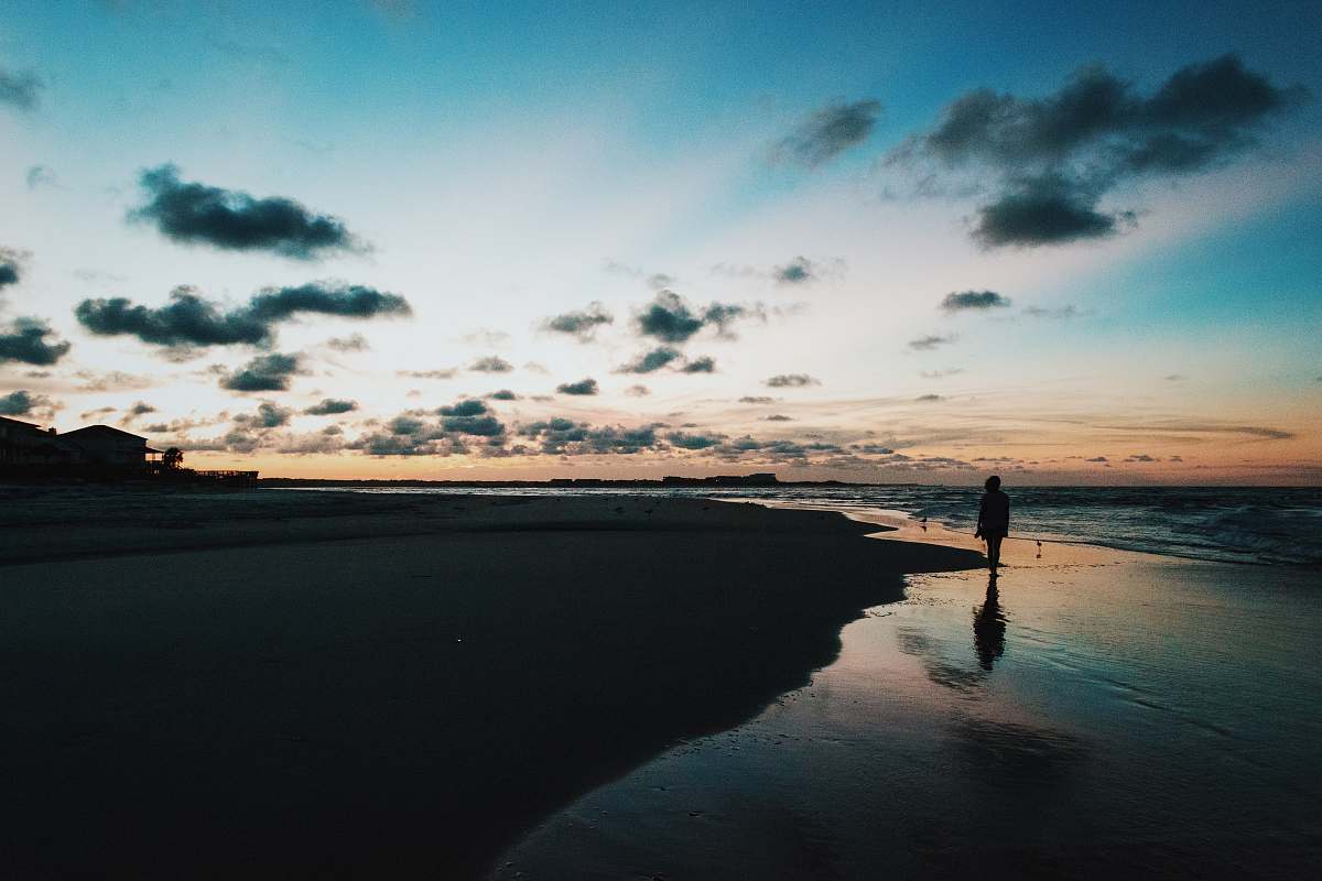 ocean silhouette of person walk through beside ocean under blue and cloudy sky during sunset sea