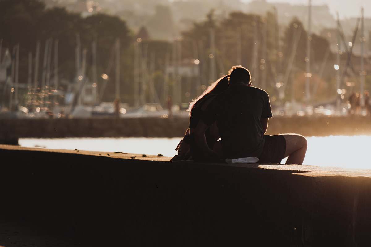 human man and woman sitting on bay near body of water during daytime person
