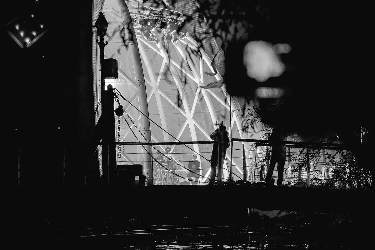 person grayscale photography of silhouette of people by building black-and-white