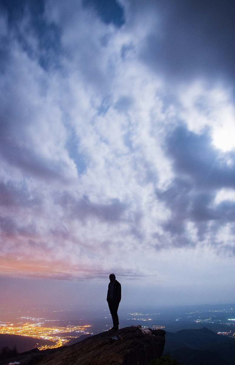 person man standing on cliff with cityscape view under cloudy sky nature