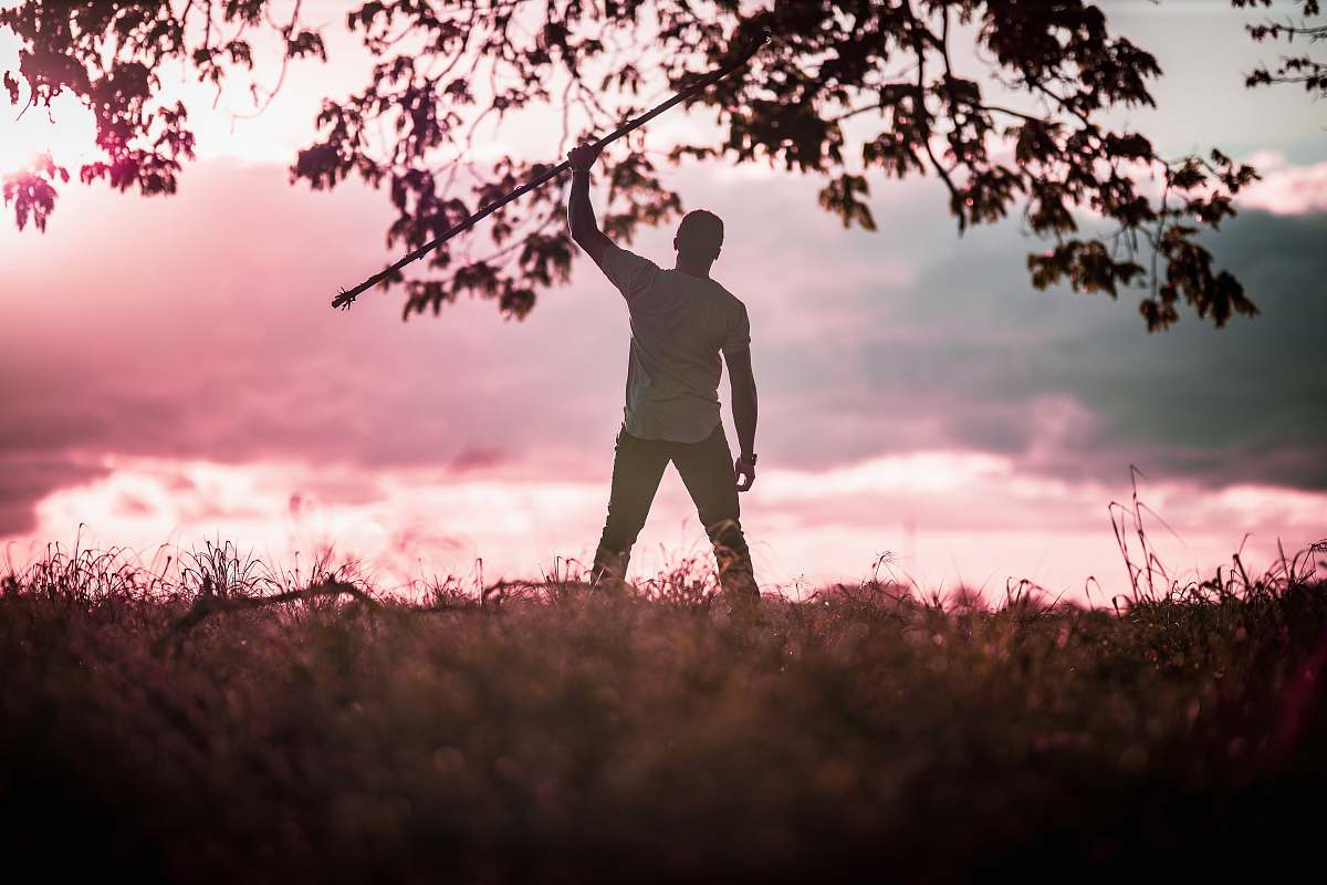 person man standing wearing white t-shirt and black pants raising right hand during daytime standing
