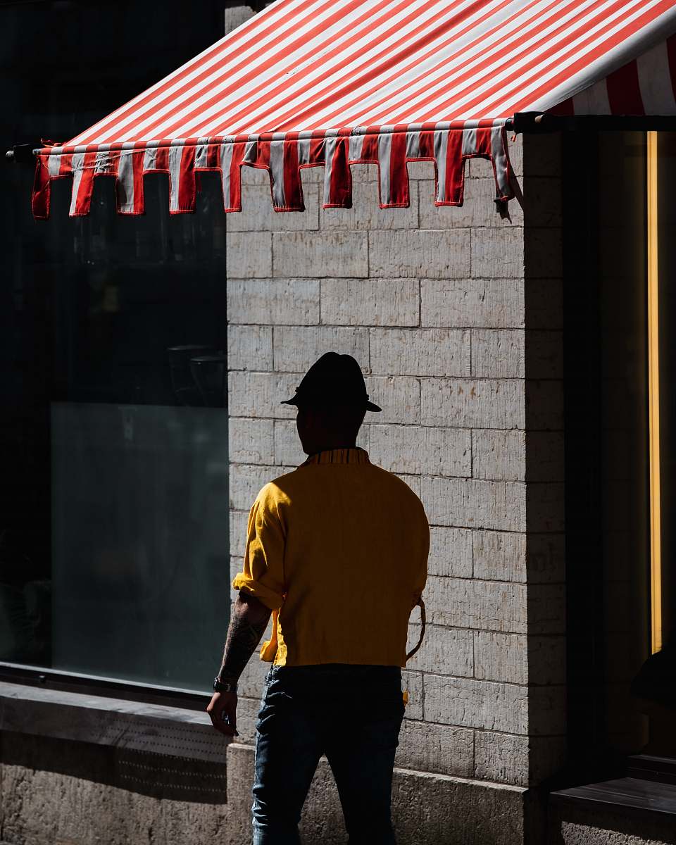 person man walking under red and white striped awning during daytime people