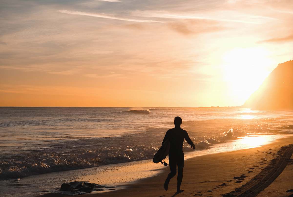 person silhouette of man carrying surfboard running on shore people