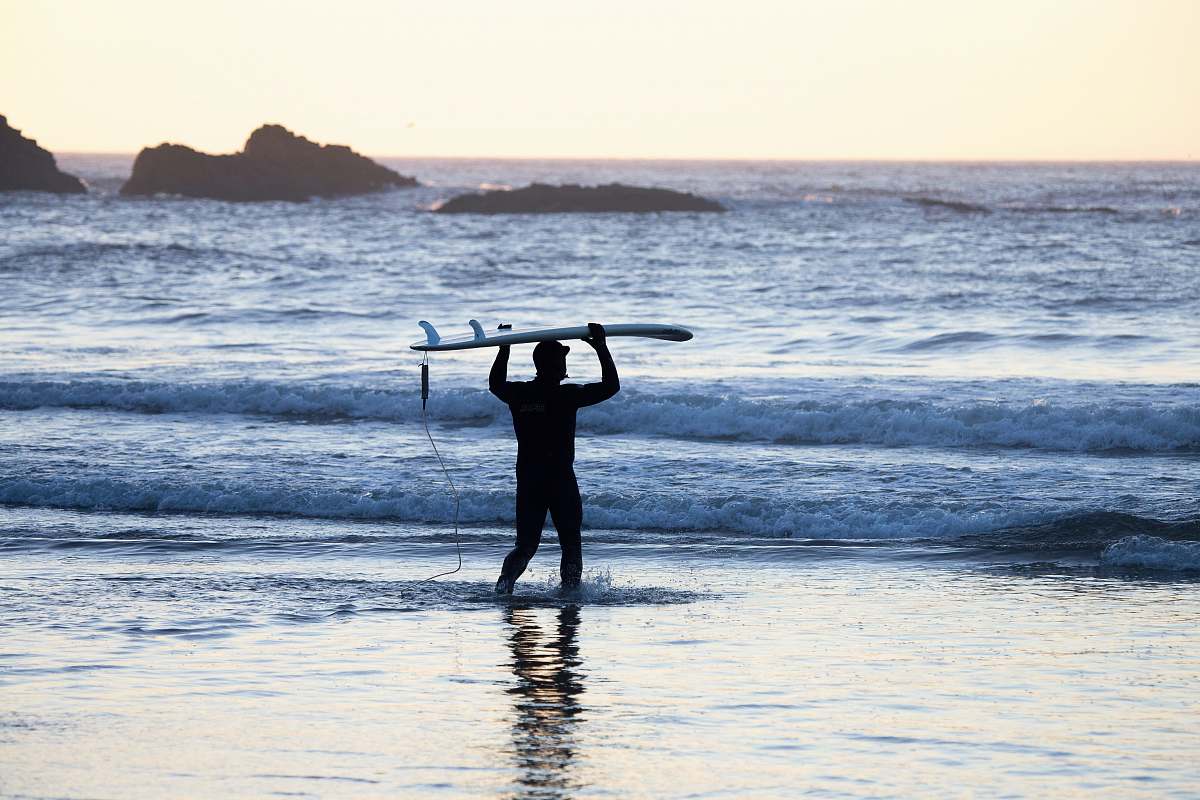 person silhouette of man holding surfing board in seashore during daytime people