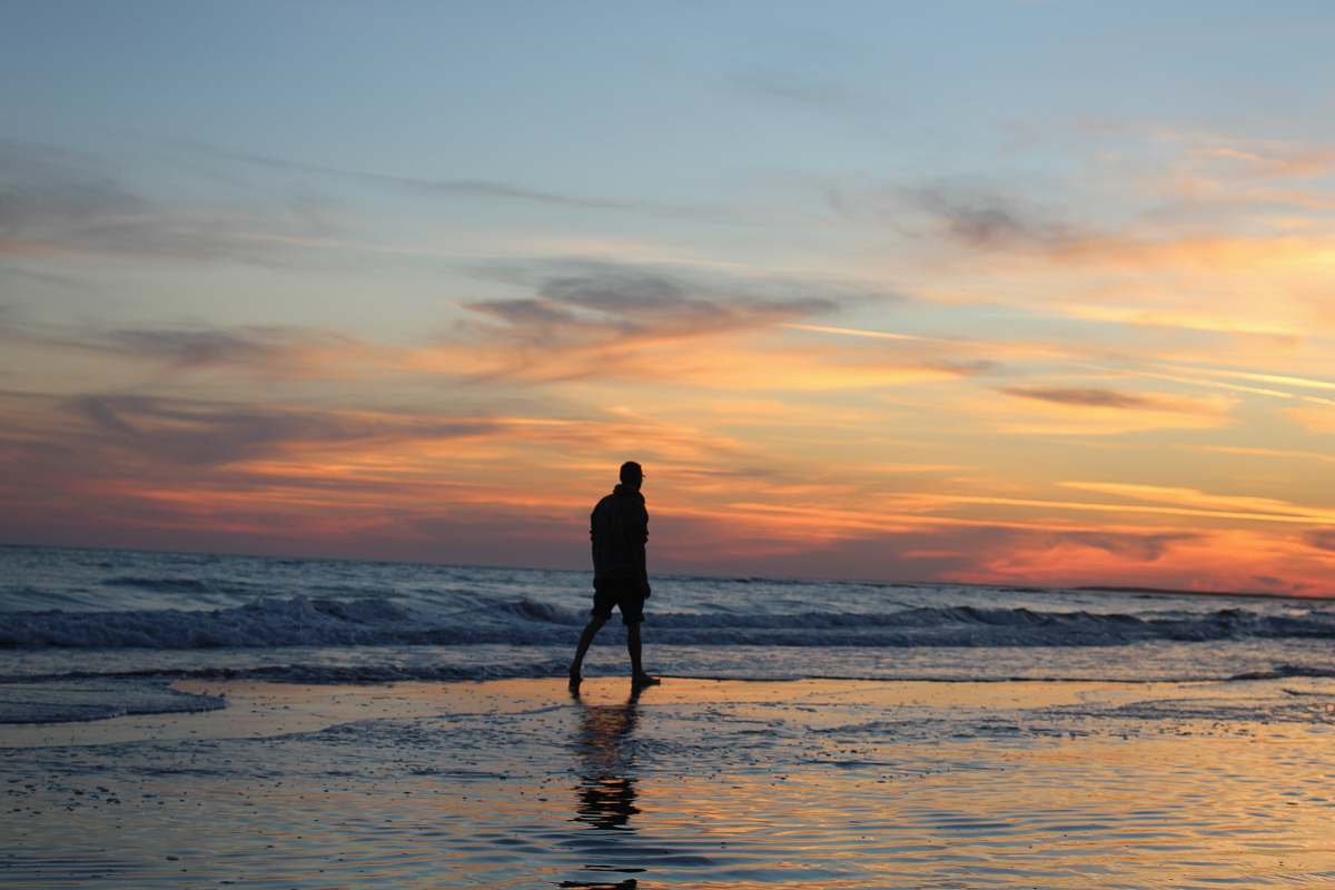 person silhouette of man walking on seashore standing
