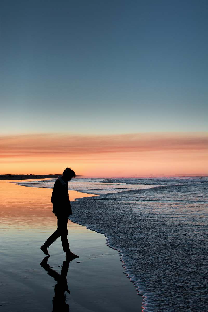 person silhouette of man walking on seashore under orange sky standing