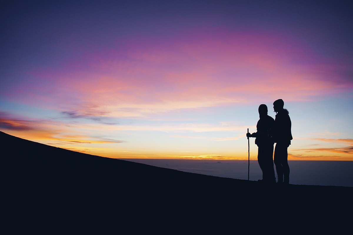 person silhouette of two man walking on top of mountain people