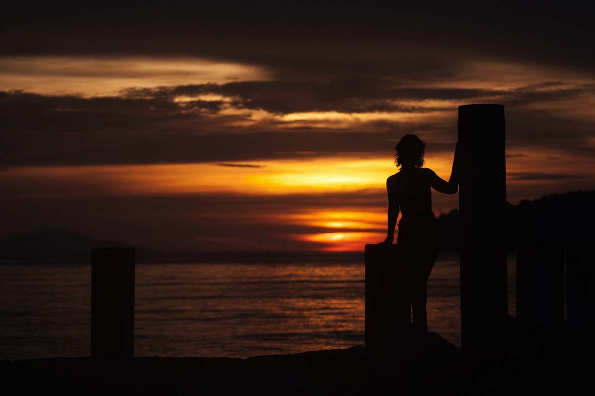 person silhouette of woman on dock during orange sunset people
