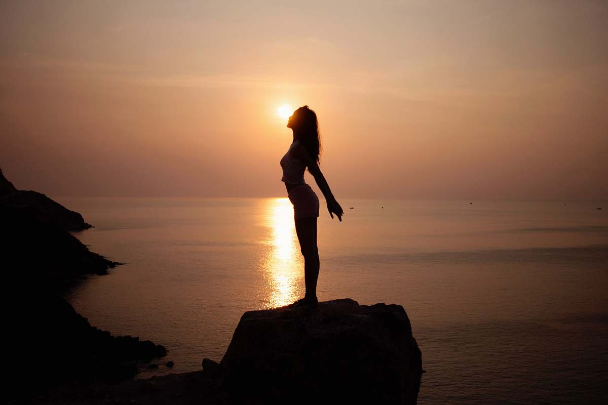 person silhouette of woman standing on sea cliff during golden hour standing