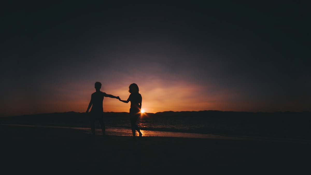 person silhouette photo of couple beside sea holding hands
