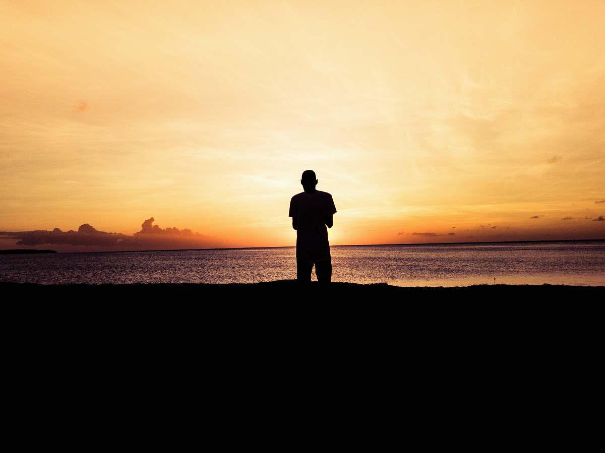 person silhouette photo of person standing in front of body of water during sunset standing