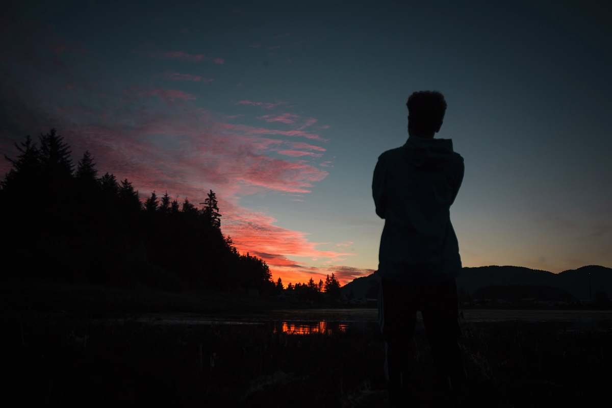 person silhouette photography of person standing in front of lake people