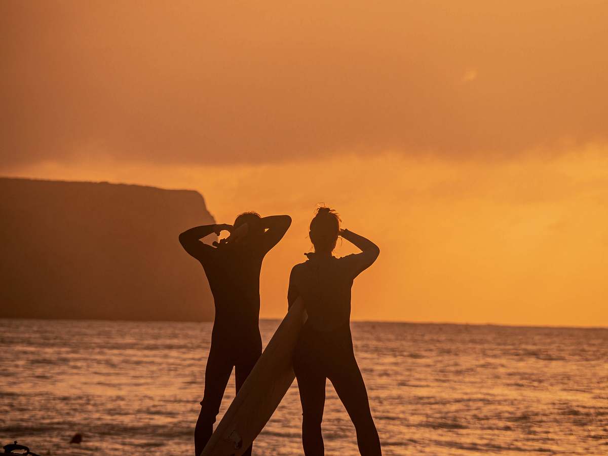 person silhoutte of person wearing wetsuit holding white surfboard standing on seashore during sunset sneery standing