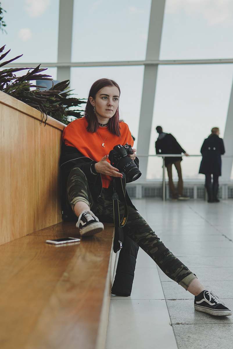 person woman holding DSLR camera while sitting on chair people