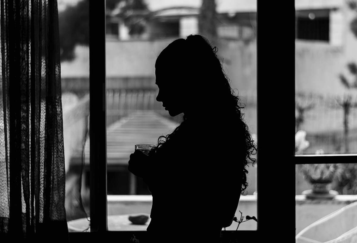 person woman inside building near window with curtain black-and-white