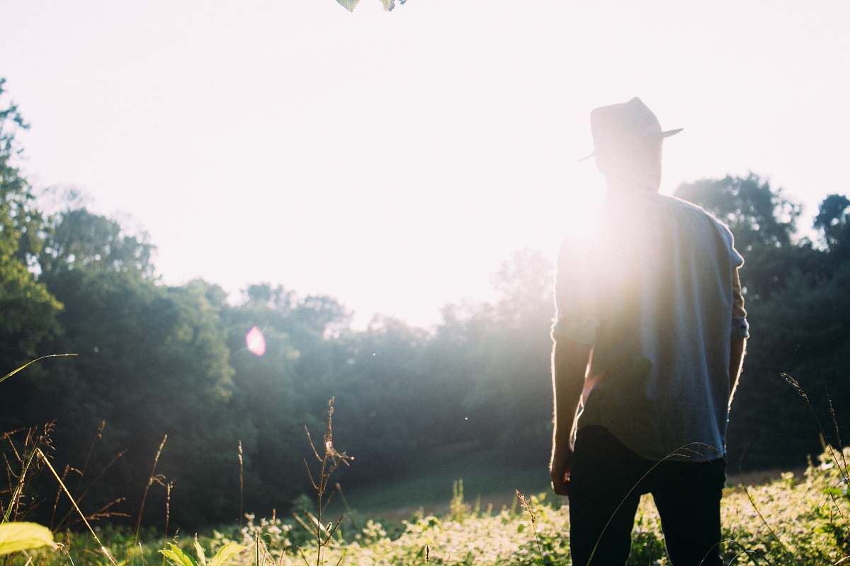 hat man standing on grass field with sun gazing people