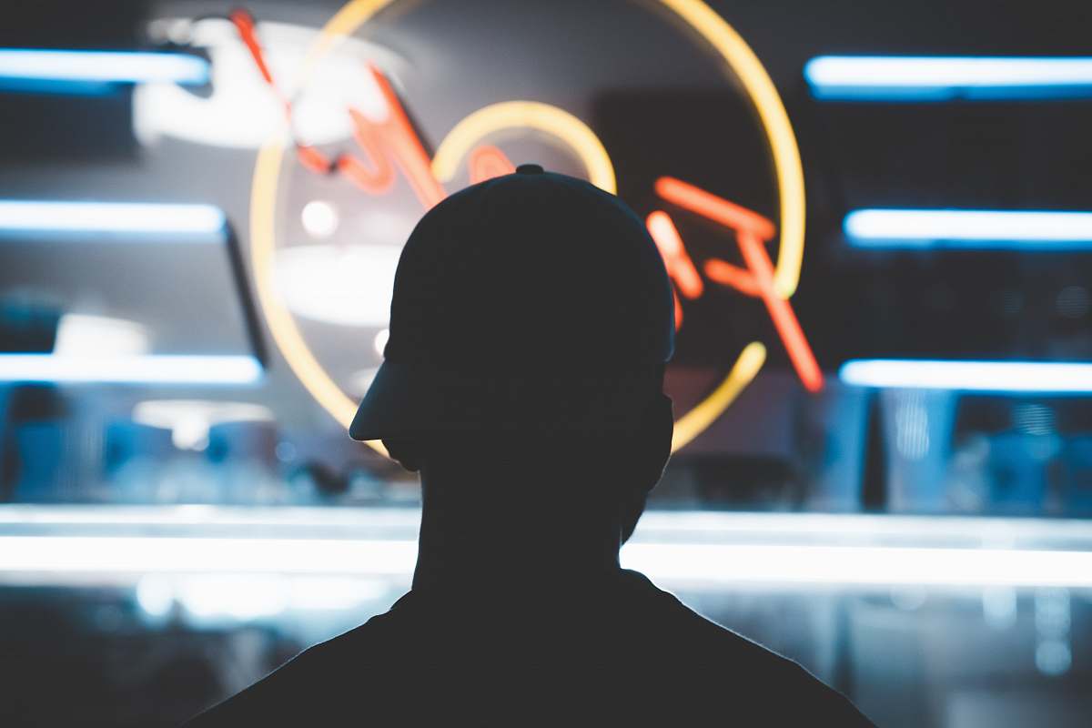 person silhouette of man wearing fit cap near LED sign silhouette