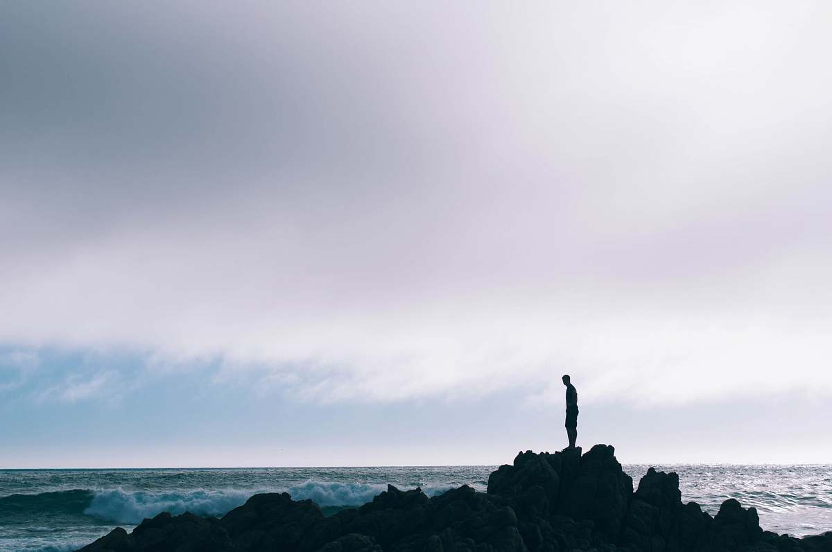 silhouette man standing on boulder in front of ocean standing
