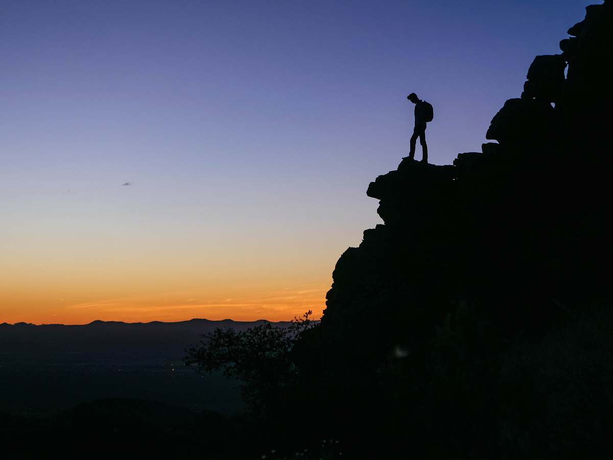 silhouette man with backpack looking overview from the cliff outdoors