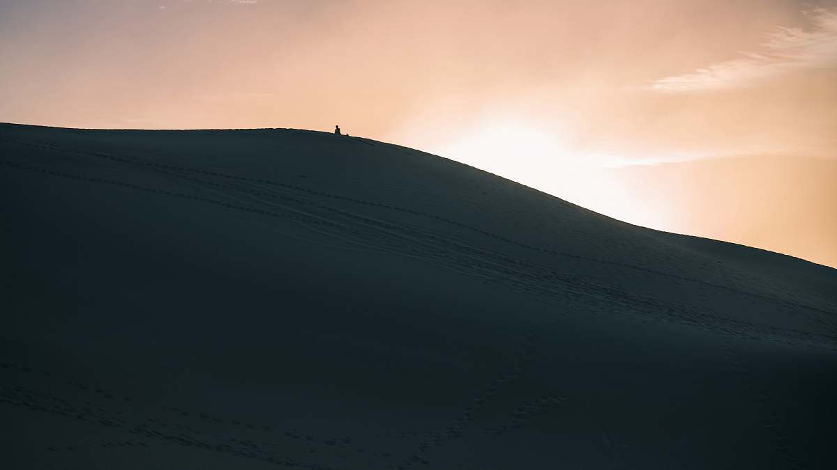 Witness the breathtaking moment of a lone figure trekking up a majestic sand dune as the sun sets on the horizon, casting warm hues across the desert landscape. This stunning image captures the essence of adventure and solitude, making it perfect for travel blogs, outdoor lifestyle articles, or inspirational posters. Ideal for those seeking to convey themes of exploration, nature, and tranquility.