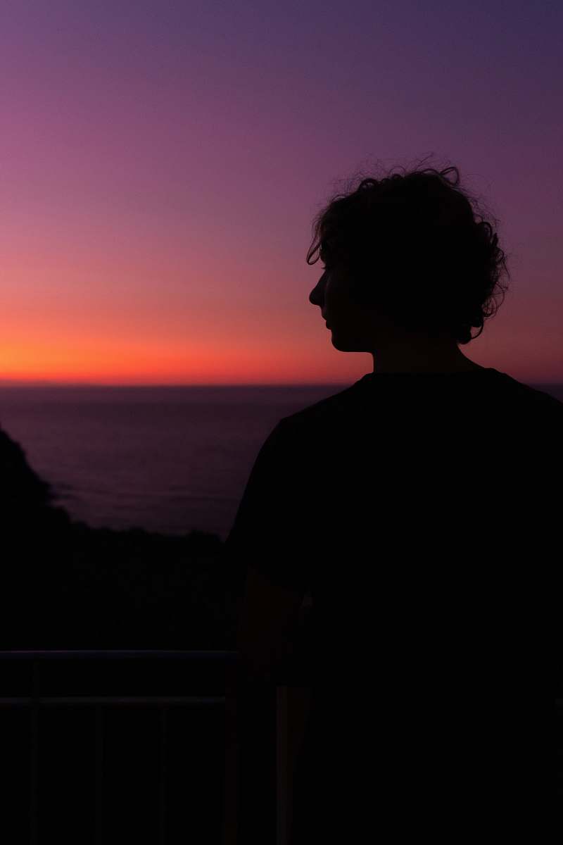 outdoors silhouette of man near body of water during golden hour sky