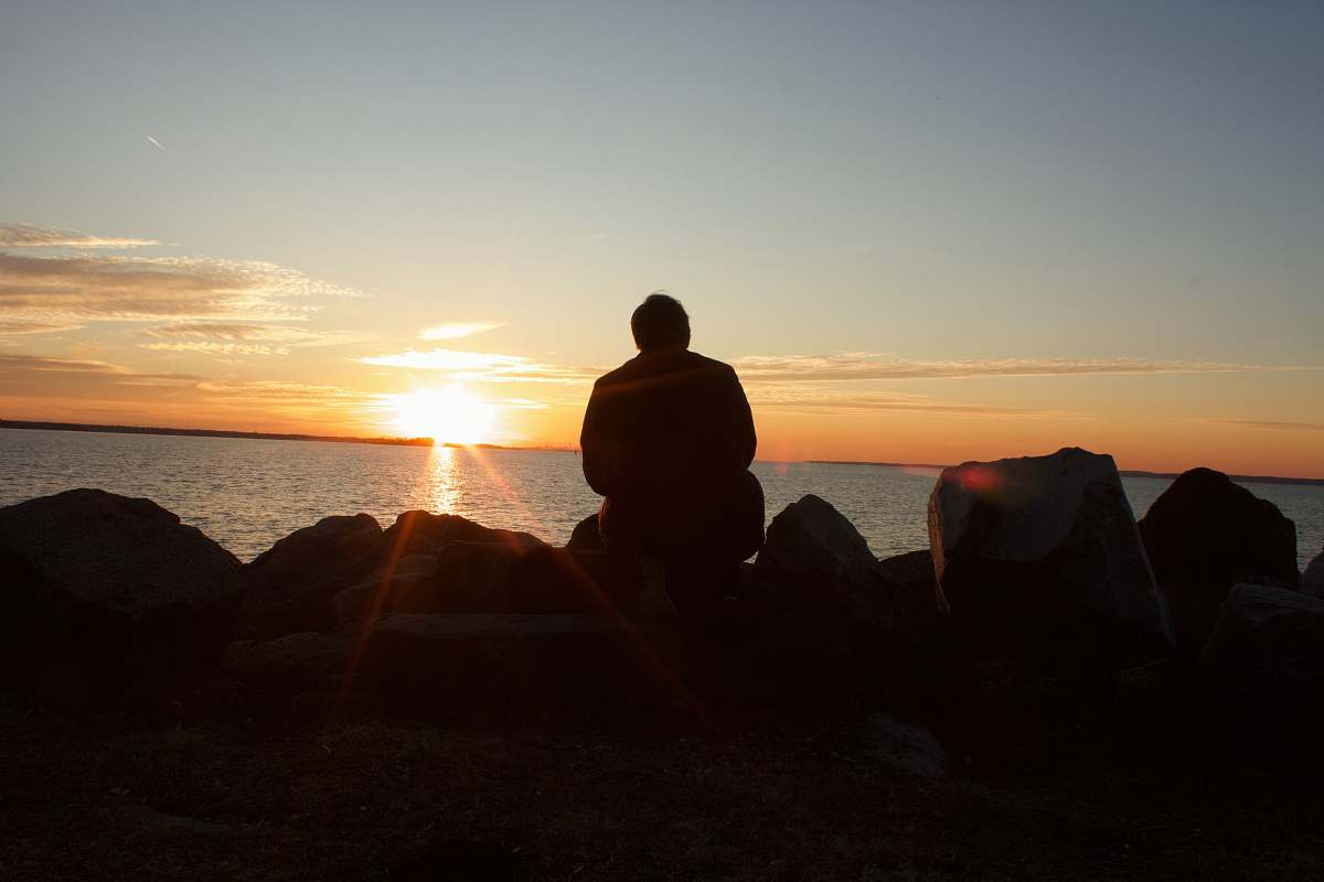 human silhouette of man sitting on rock during sunset person