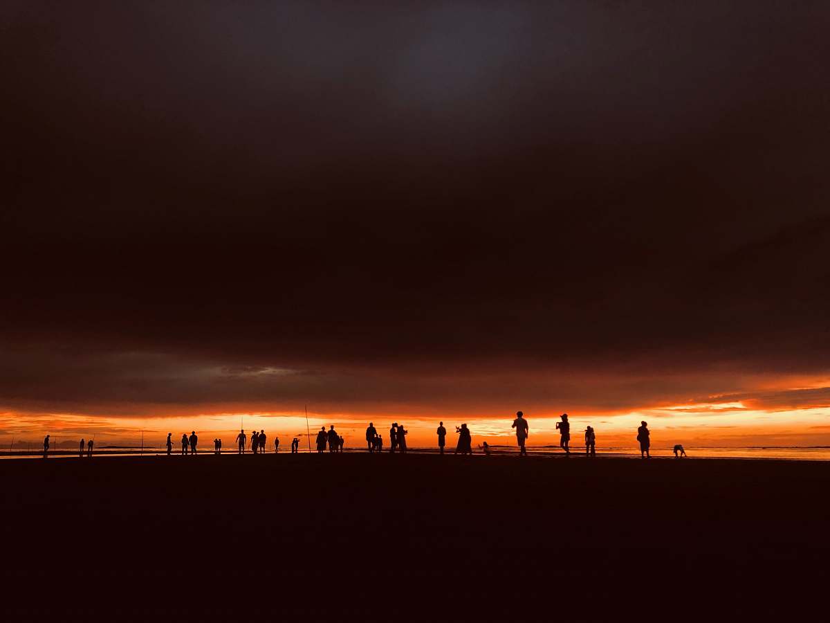 human silhouette of people standing under dark clouds during golden hour person