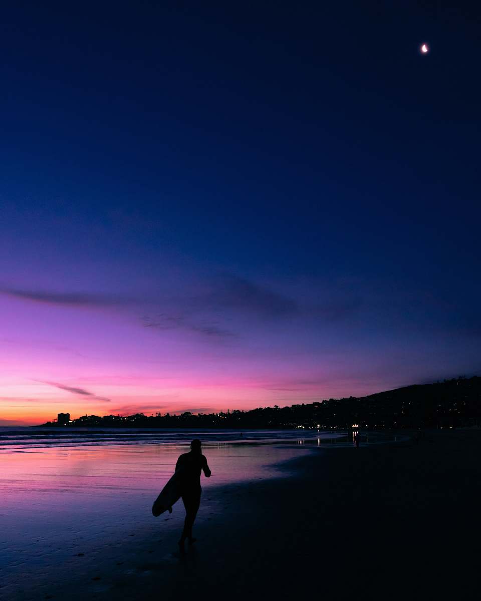 person silhouette of person carrrying surfboard while walking on seashore sky