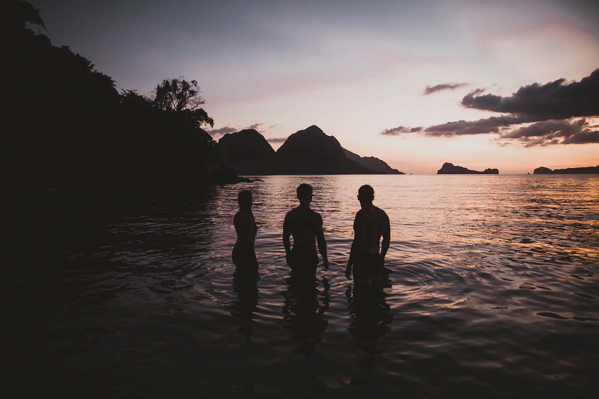 human silhouette of three person standing on calm body of water person