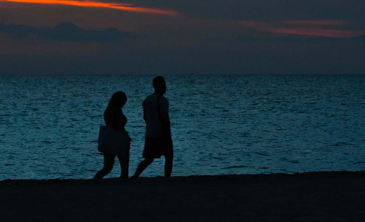 human silhouette of two person walking beside beach person