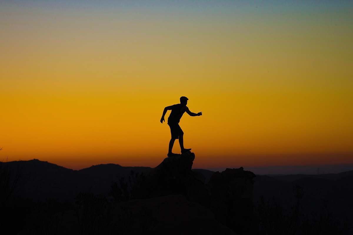 sunset silhouette photo of person on mountain cliff sunrise