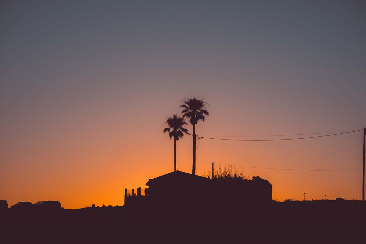 outdoors silhouette photography of house near palm tree during golden hour sunset